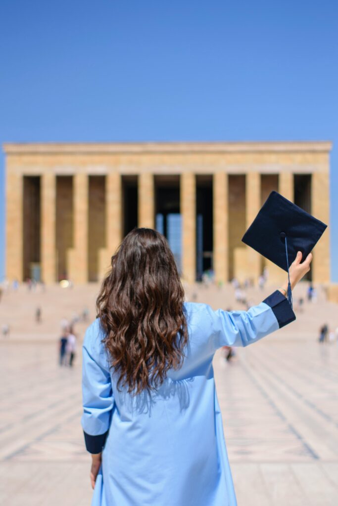 Graduating woman in blue gown celebrates in front of Anıtkabir, Ankara.